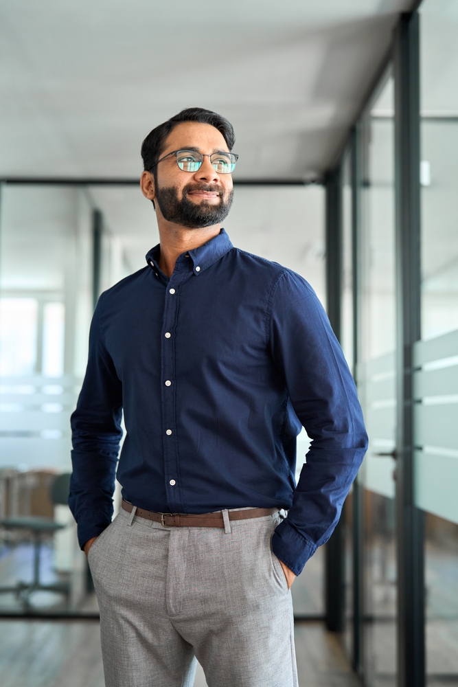 Confident Indian business man leader looking aside standing in office.