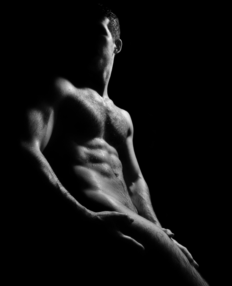 nude man seated mostly in the shadows