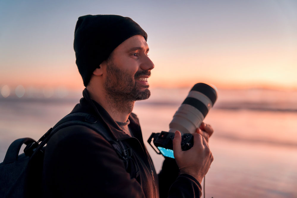 latin mature photographer holding professional camera on the beach and smiling happy portrait