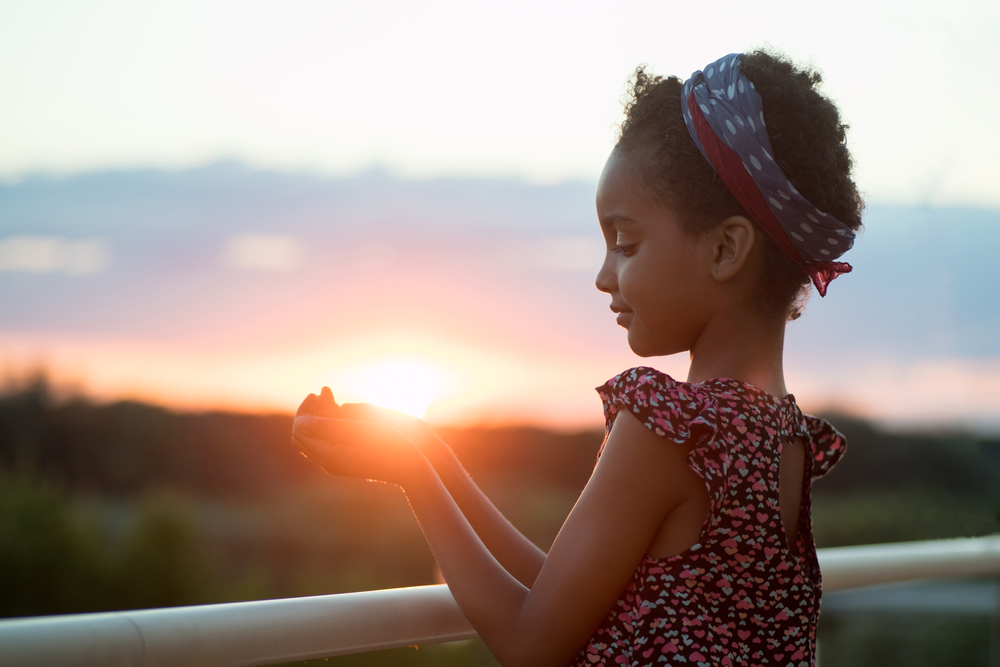 Portrait of a girl at sunset. Child holds the sun in her hand.
