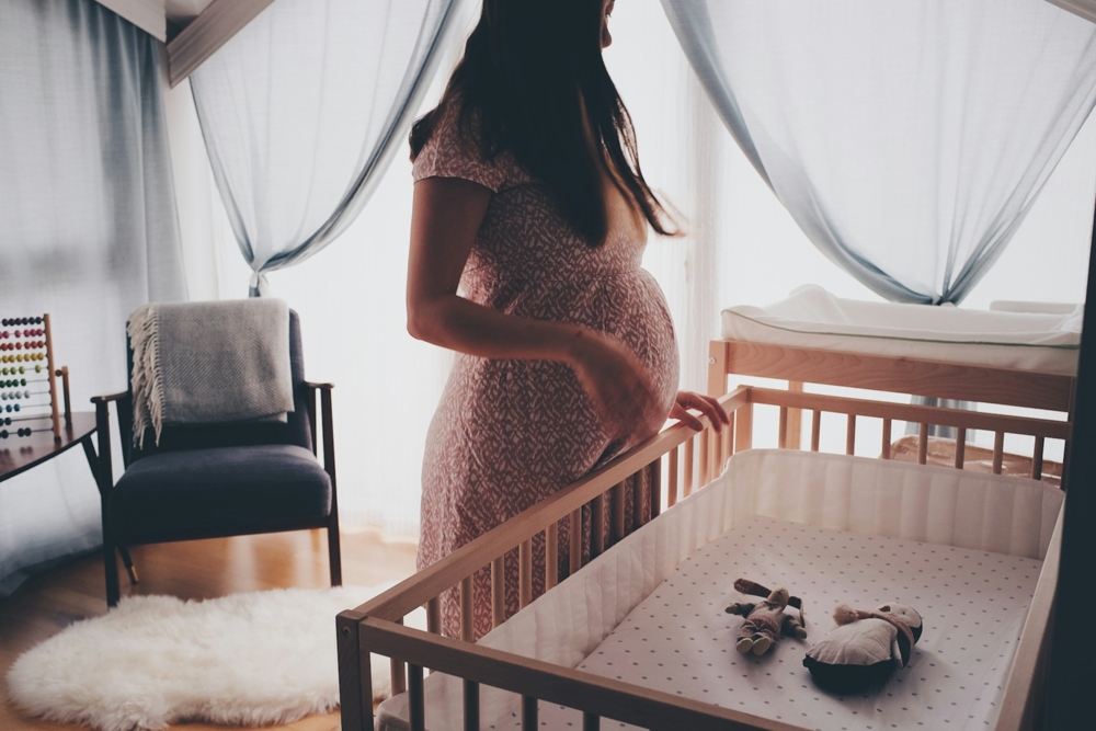 Pregnant woman standing beside wooden crib