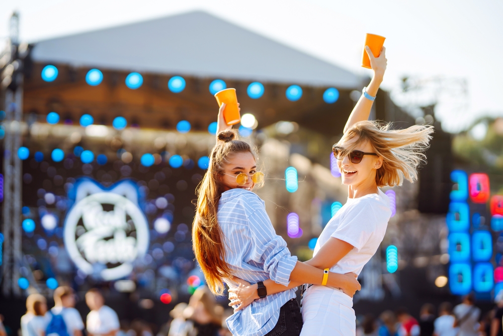 Two women holding yellow cups at am outdoor concert