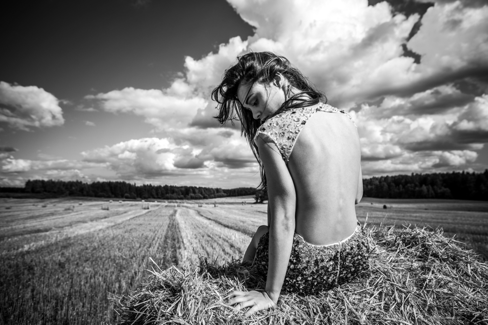 Woman sitting of hay in a field wearing a backless dress BW